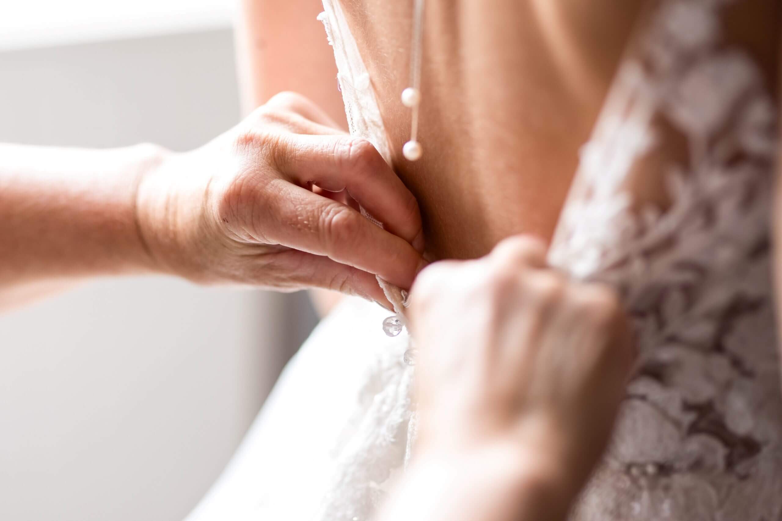 Instant Emotion : gros plan sur la fermeture des derniers boutons de la robe de mariage par la mère de la mariée.